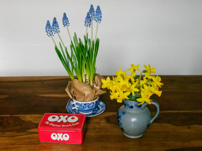 Spring flowers arranged in ceramic vessels on a wooden surface with a red box.
