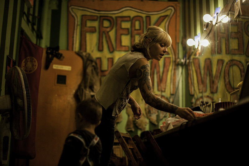 Performer leaning over audience member in dimly lit venue with neon signage.