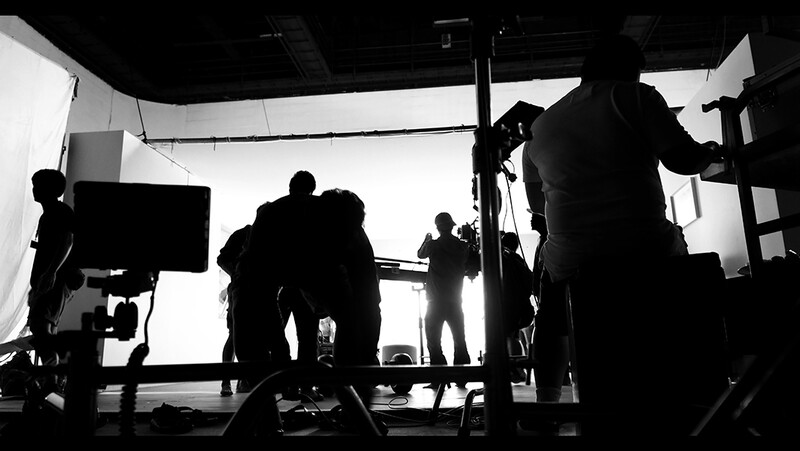 Silhouetted film crew members on a production set with bright backlighting and studio equipment.