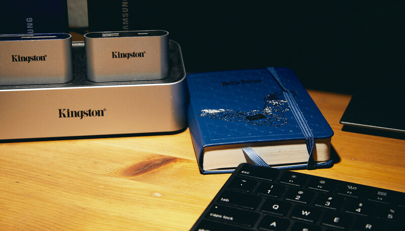 Kingston storage devices and a blue notebook arranged on a wooden desk next to a black keyboard.