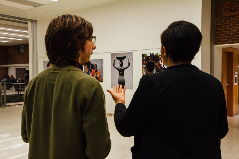 Two people viewing portrait photographs displayed on a white wall in an indoor gallery space.