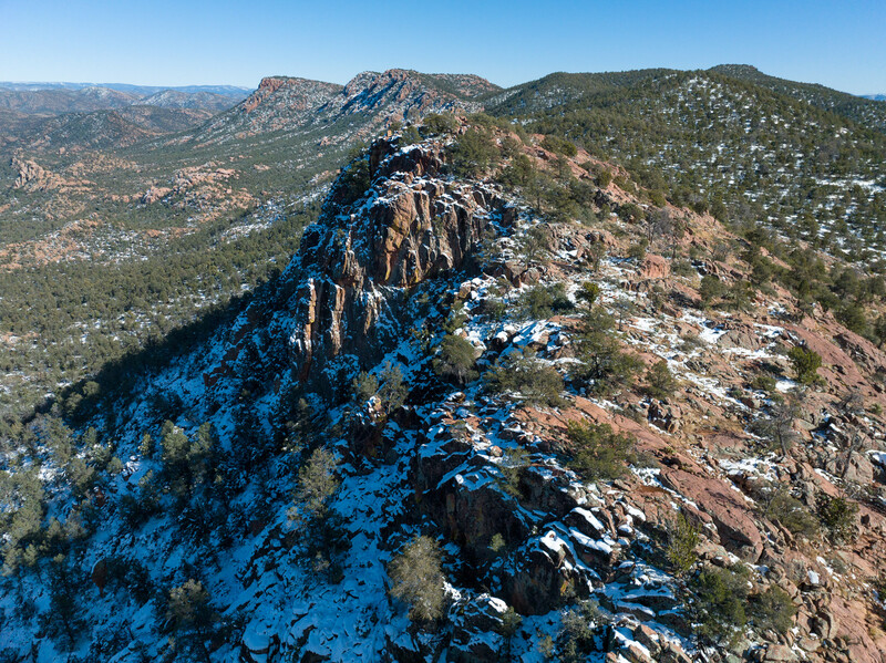 Aerial view of a rocky ridge covered in patchy snow with forested valleys below.