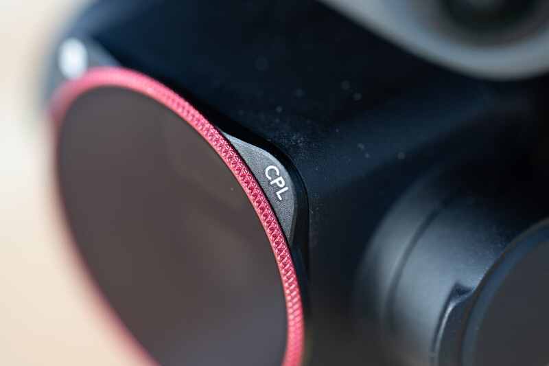 Close-up of a camera lens filter with pink ribbed rim and dark glass element.