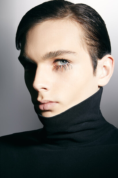 Profile portrait of a person with dark hair wearing a black turtleneck against a neutral gray background.
