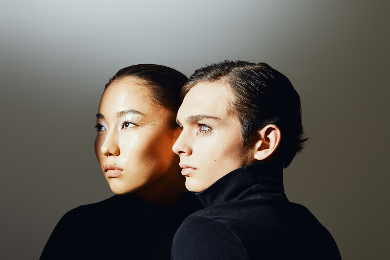 Two figures in profile against neutral background, lit with warm and cool directional light creating strong shadows.