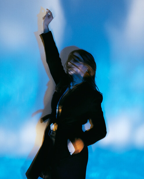 Person in dark blazer with fist raised against blue-tinted sky with clouds.