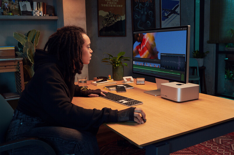 Person seated at wooden desk working at computer in dimly lit home studio space.
