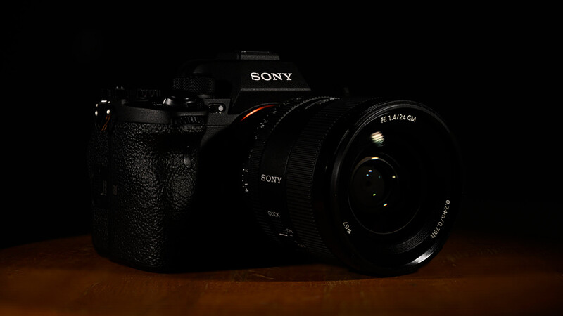 Sony mirrorless camera with attached lens on warm-toned wooden surface against dark background.