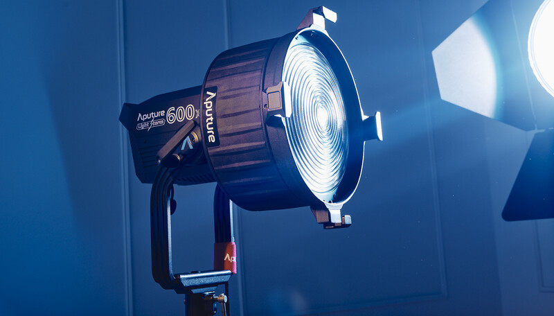 Professional studio light with Fresnel lens mounted on stand, emitting bright warm glow against blue backdrop.