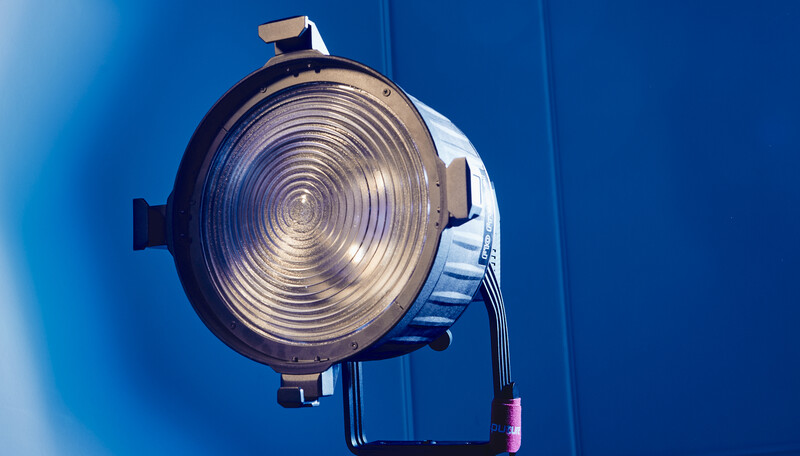 Studio spotlight with concentric Fresnel lens facing camera against vibrant blue backdrop.