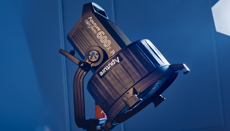 Profoto B10 Plus monolight with reflector and diffuser attachment against blue background.