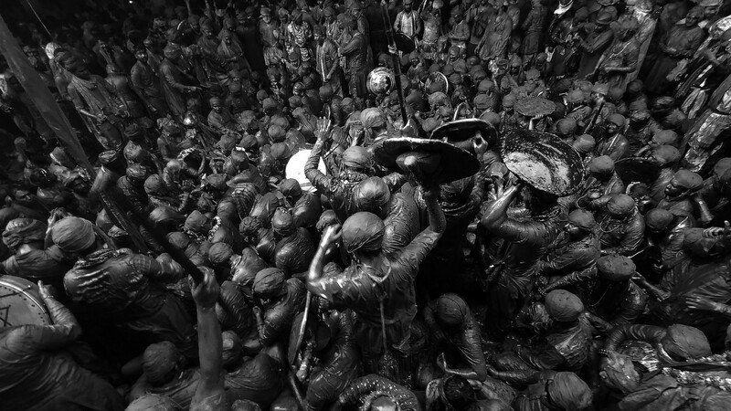 Large crowd of mud-covered people engaged in a chaotic festival or celebration, shot from above in black and white.