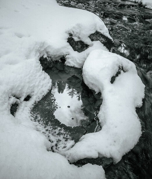 Snow-covered rocks frame a dark flowing stream in winter.