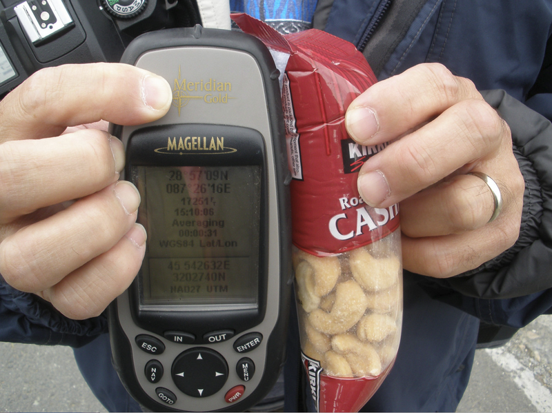 Hands holding a Magellan GPS device and a bag of nuts outdoors.