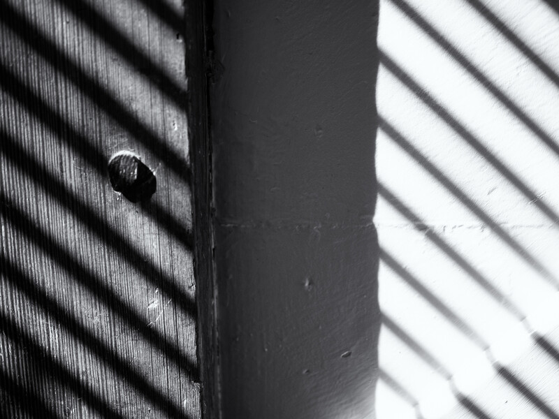 Dark cylindrical post with dramatic diagonal shadow lines cast across adjacent light and dark surfaces.
