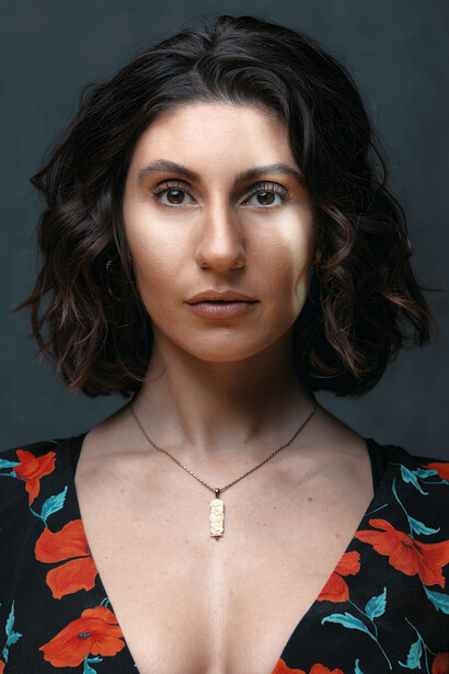 Portrait of woman with shoulder-length dark wavy hair wearing floral print top against neutral backdrop.