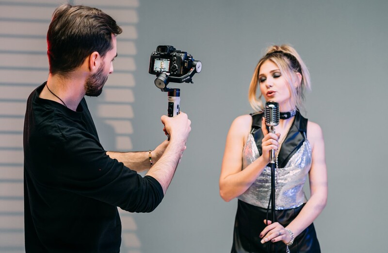 Cameraman operating a gimbal-mounted camera while recording a woman speaking into a microphone during an interview or broadcast.