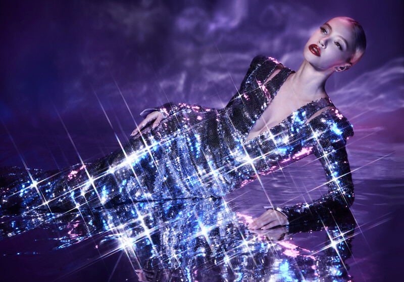 Person in sequined black jacket posed against purple sky with digital city light overlay effect.