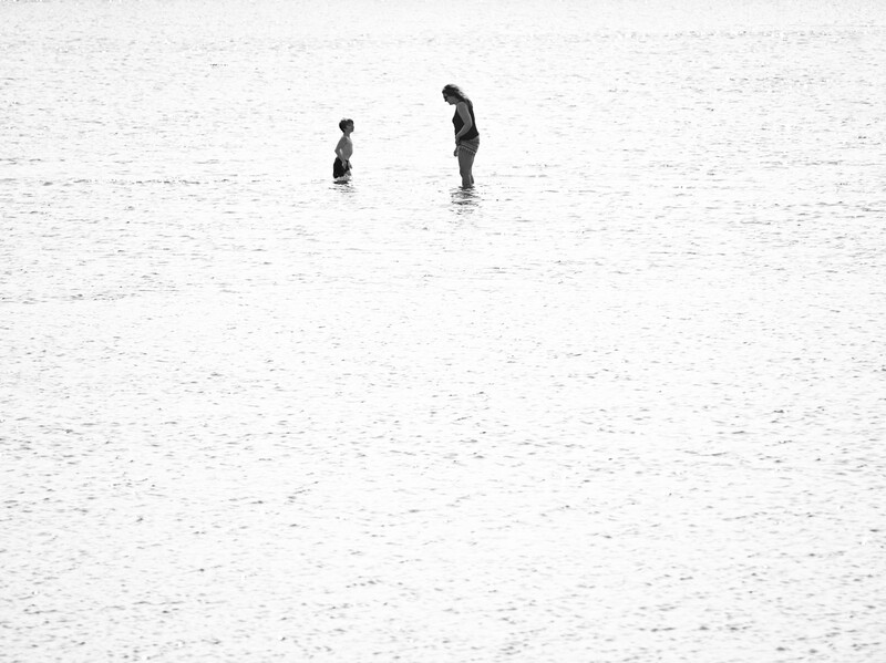 Two figures standing in shallow water on a vast, textured beach at low tide.