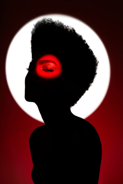 Silhouette portrait with glowing red eye against bright circular backlight.