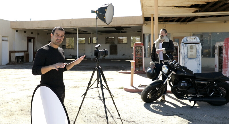 Cinematographer operating camera on tripod during outdoor film production at abandoned gas station.