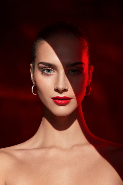 Woman's face split by red lighting against dark background, dramatic studio portrait.