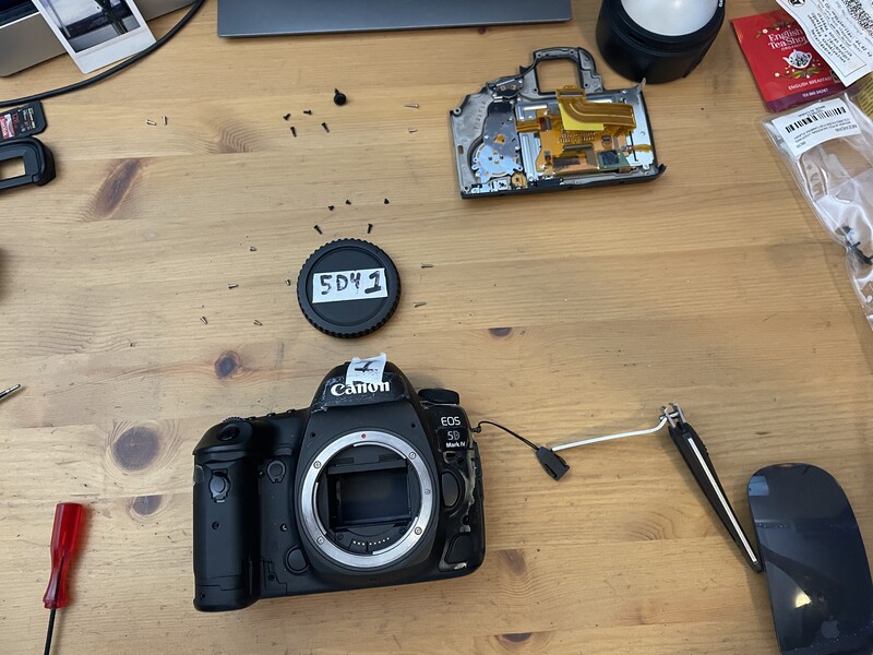 Canon EOS 5D Mark IV camera body displayed disassembled on wooden work surface with internal components.