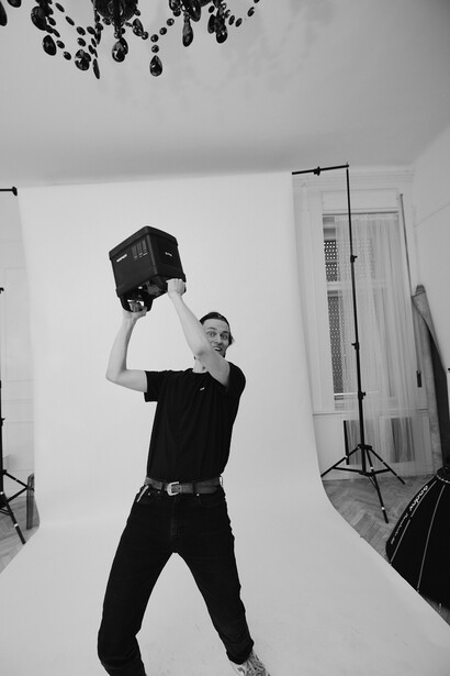 Studio portrait of person in black clothing holding large black studio light overhead during shoot.