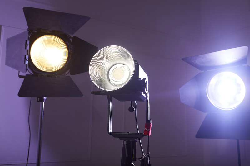 Three professional studio lights mounted on stands with warm and cool color temperatures illuminating a purple-tinted backdrop.