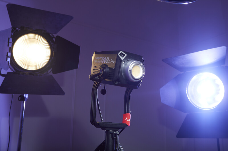 Three professional LED film lights mounted on stands against a purple backdrop, with barn doors and focusing mechanisms visible.