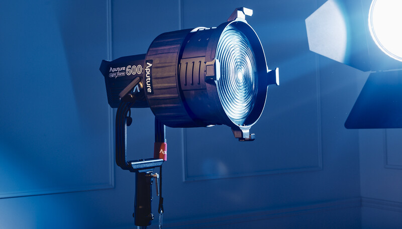 Professional studio spotlight with Fresnel lens mounted on stand, glowing intensely against dark blue backdrop.