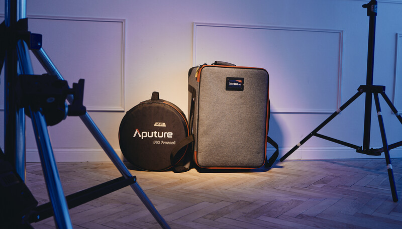 Photography lighting equipment including an Aputure light, carrying case, and tripod stands arranged on a wooden floor.