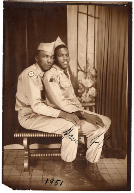 Two people in light-colored uniforms sitting together on a bench, smiling at the camera.