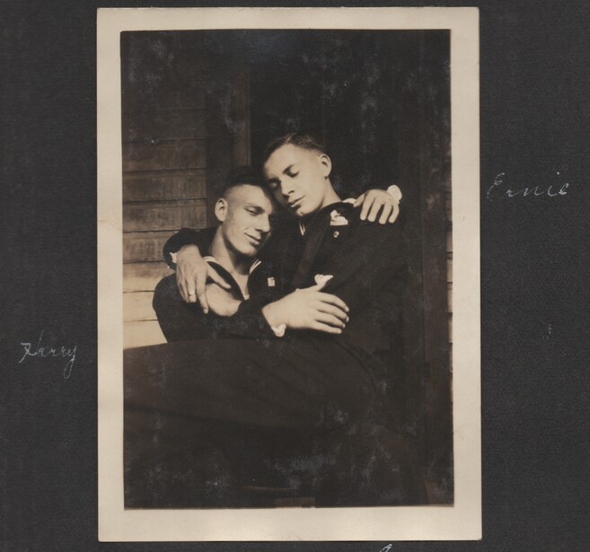 Two young men in dark jackets embracing against a brick wall in a vintage black and white portrait.