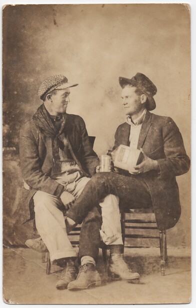 Two men in period clothing seated and facing each other in conversation.