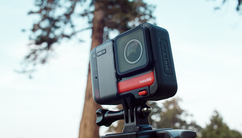 Action camera mounted on a pole against a blurred forest and sky background.