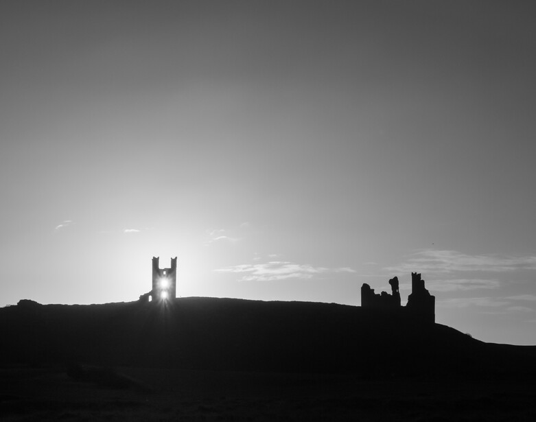 Silhouetted ruins of stone structures against a bright sky on a hilltop horizon.