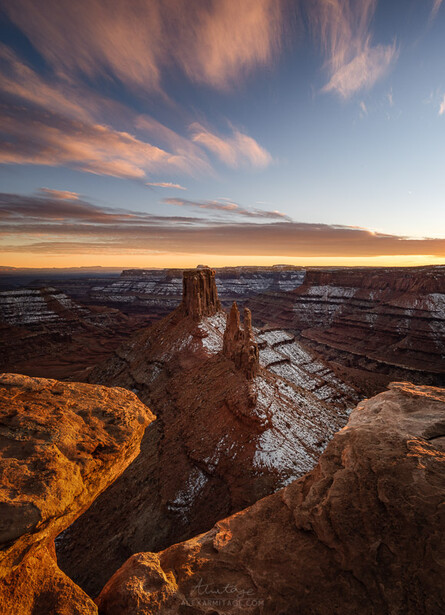 Desert rock formations silhouetted against a golden sunset sky with wispy clouds.