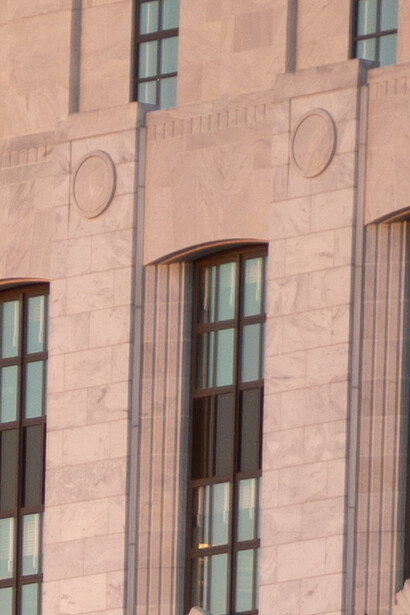 Terracotta-colored building facade with tall rectangular windows and circular decorative elements.