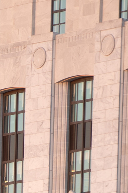 Modernist building facade with vertical rectangular windows and circular decorative elements in terracotta stone.