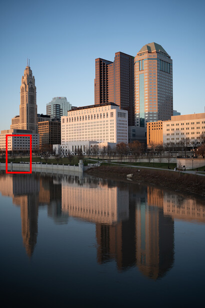 Downtown skyline reflected in calm river water at golden hour with clear blue sky.