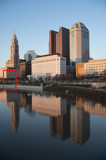 Downtown skyline reflected in still water at golden hour with warm light on buildings.