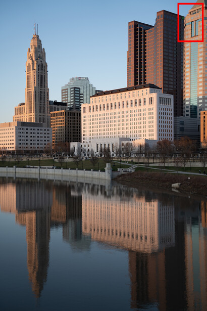 Urban skyline reflected in still water at sunrise, with historic and modern buildings lining the riverfront.