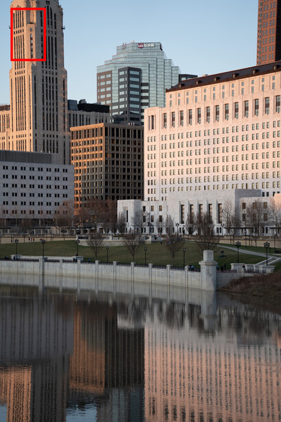 Urban waterfront skyline with brick and glass buildings reflected in still water at golden hour.