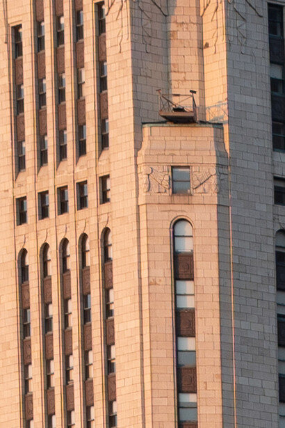 Warm sunlight illuminates a narrow vertical tower with arched windows set between two tall rectangular buildings.