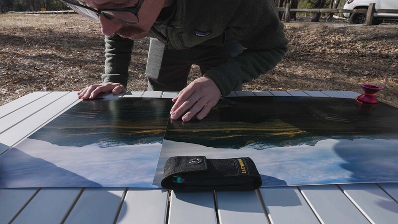 Photographer inspecting a large print or transparency on a lightbox in outdoor setting.