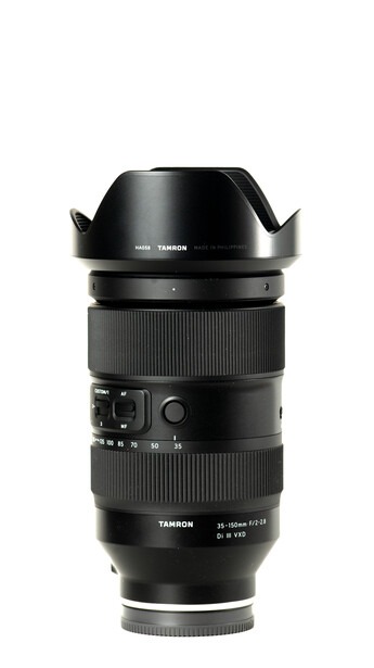 Telephoto zoom lens with black barrel, ribbed focus ring, and detached petal-shaped lens hood.