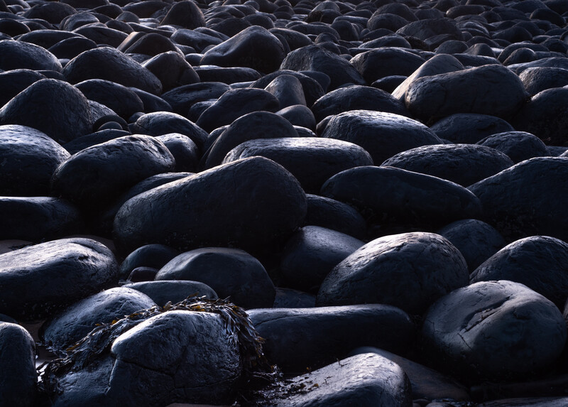 Densely packed dark rounded boulders with weathered surfaces illuminated by directional light.