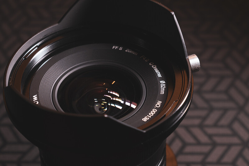 Wide-angle lens with hood attached, shot from above against a textured dark surface.