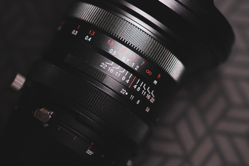 Close-up of a vintage manual focus lens showing aperture and focus ring markings against a dark background.